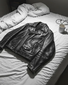 A phone snapshot of a leather jacket dumped on an unmade bed in a dim bedroom